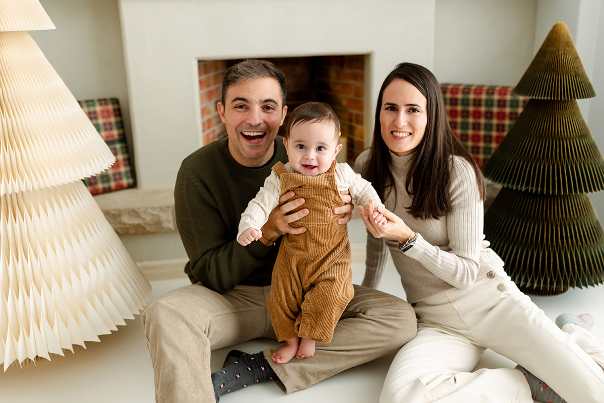 Familia posando sonriente con fondo de árboles de Navidad y chimenea