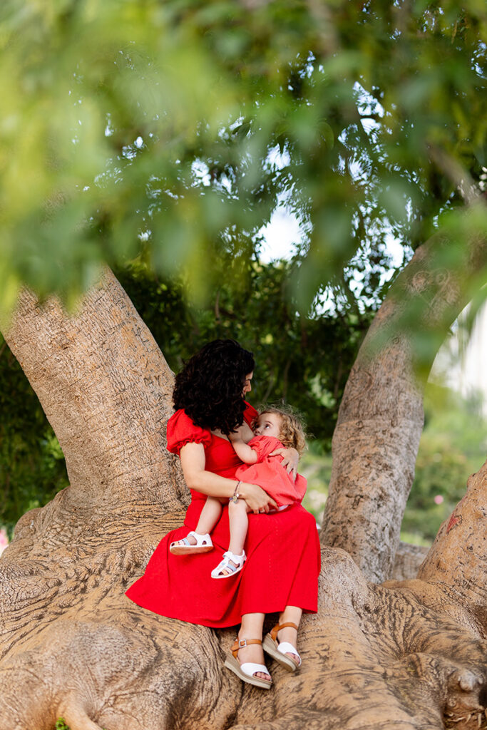 Madre dando pecho a su hija sentadas en un árbol