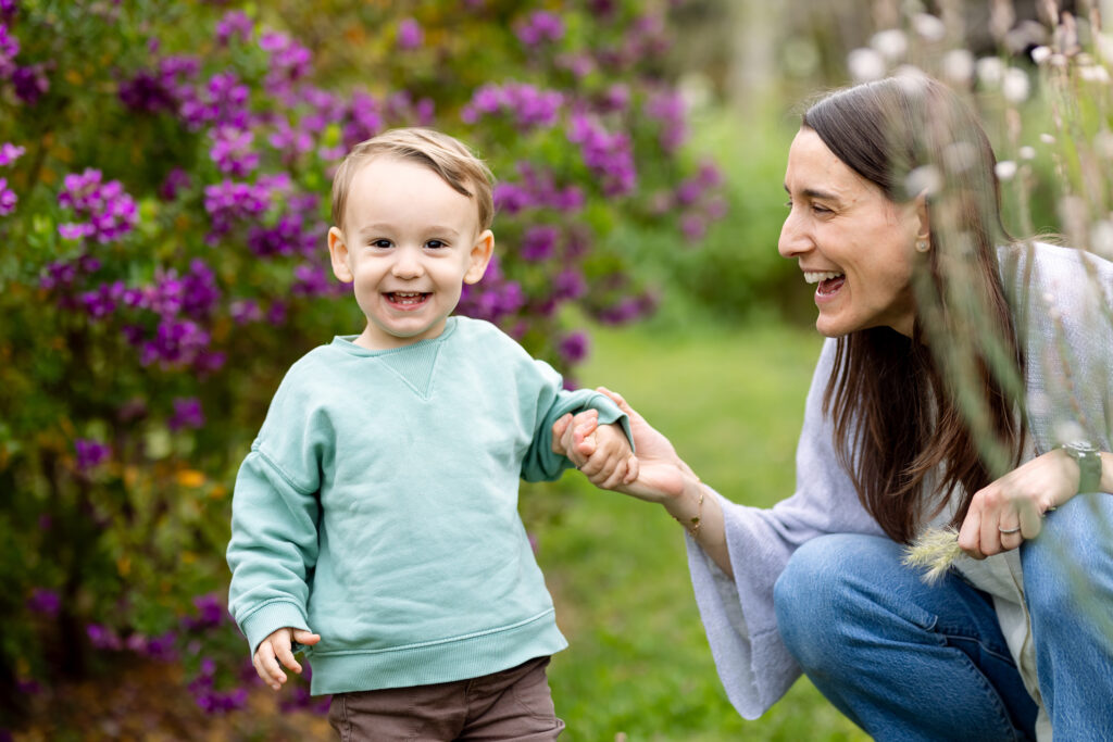 Madre aguantando mano a su hijo sonriente de 2 años en un parque