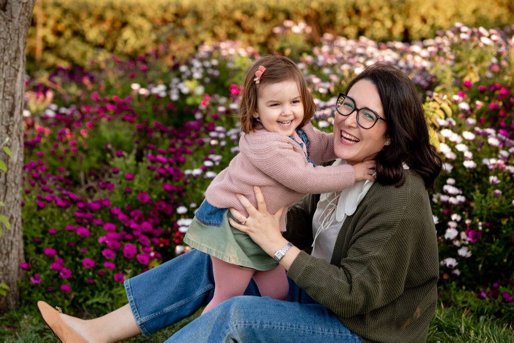 Madre abrazando a su hija y sonriendo con muchas flores de fondo