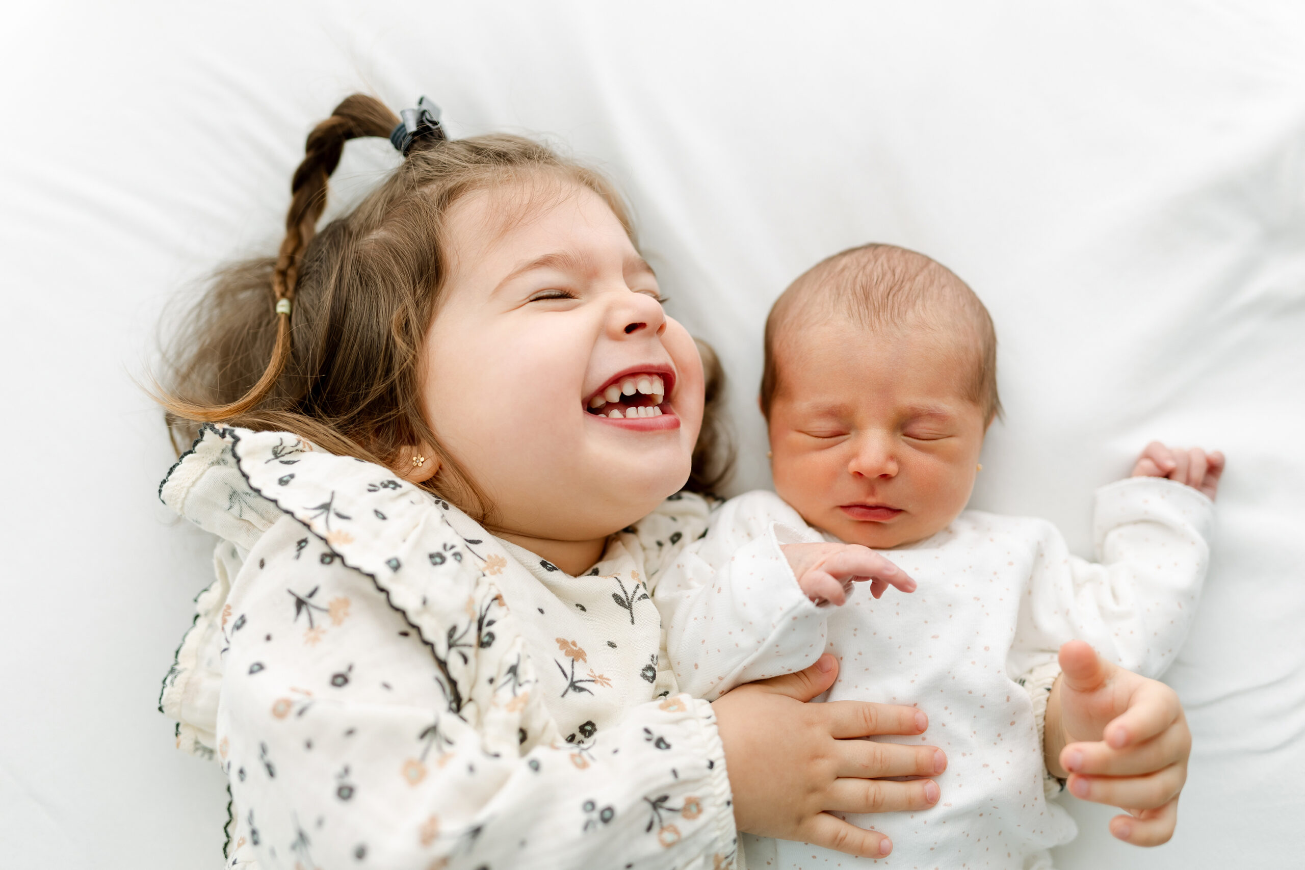 Niña riéndose mientras coge a su hermana recién nacida