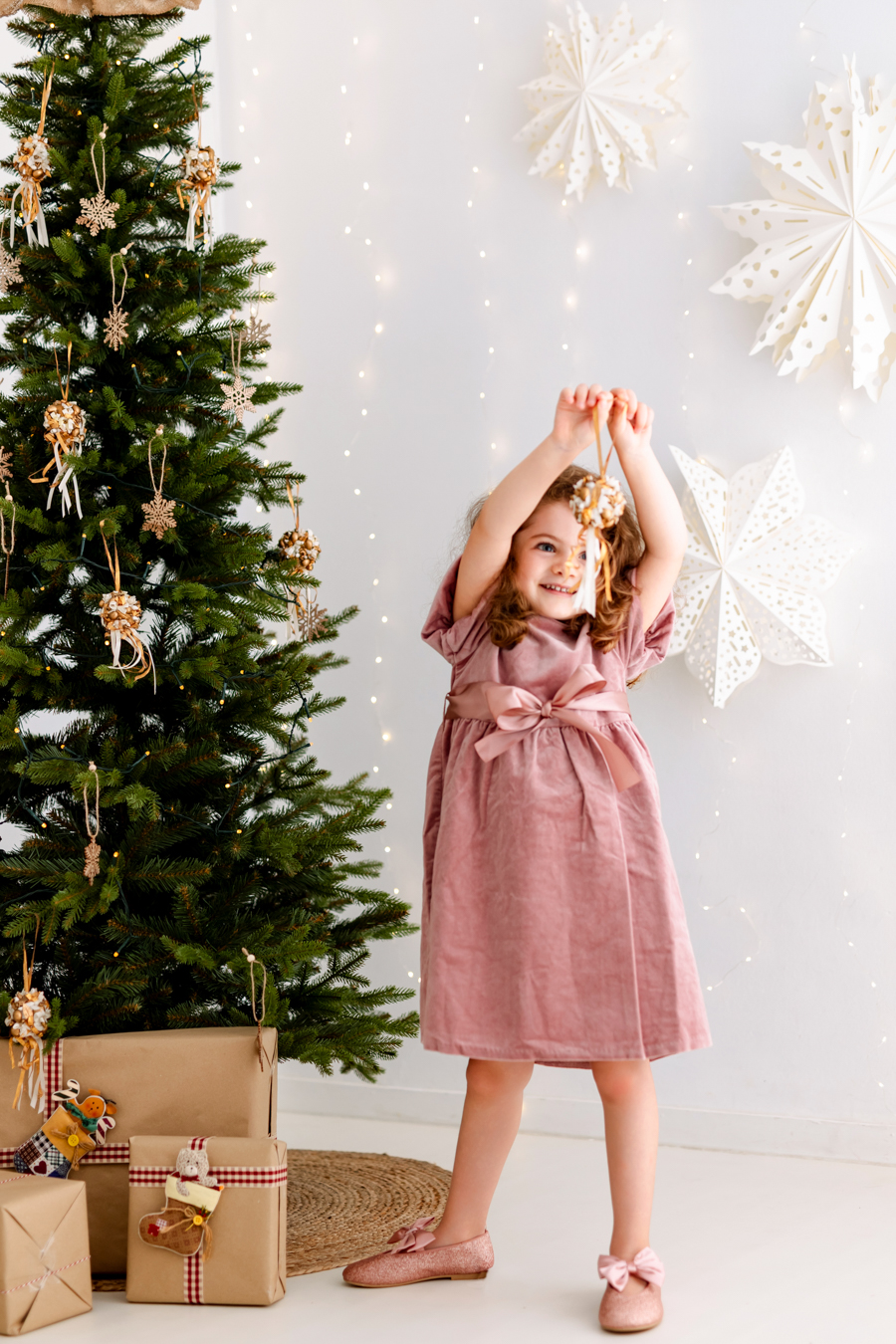 Niña con vestido rosa cogiendo un adorno del árbol de Navidad