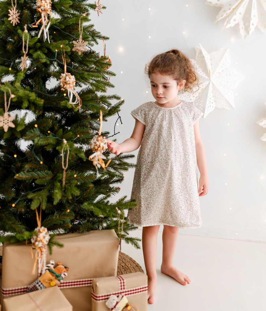 Niña cogiendo adorno de un árbol de Navidad con regalos en el suelo