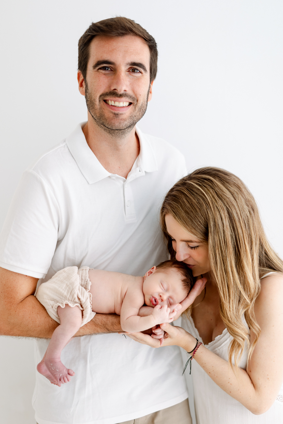 Retrato familiar en Barcelona con padres sosteniendo y acariciando a su bebé recién nacido en una sesión de fotos newborn natural.