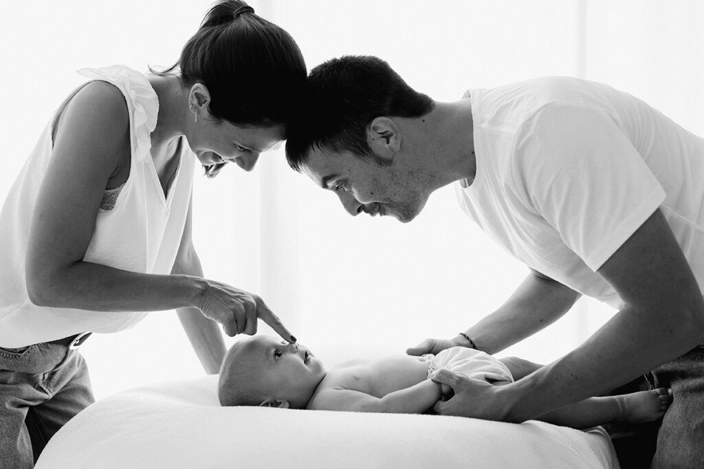 Fotografía a contraluz de papás jugando con bebé de meses