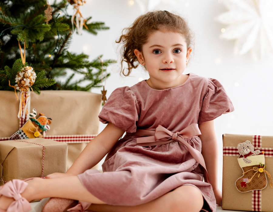 Niña mirando a cámara con árbol de navidad y regalos de fondo