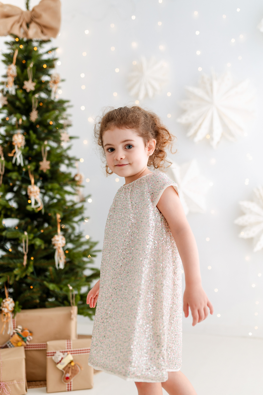 Niña con vestido lentejuelas y árbol y luces navideñas de fondo