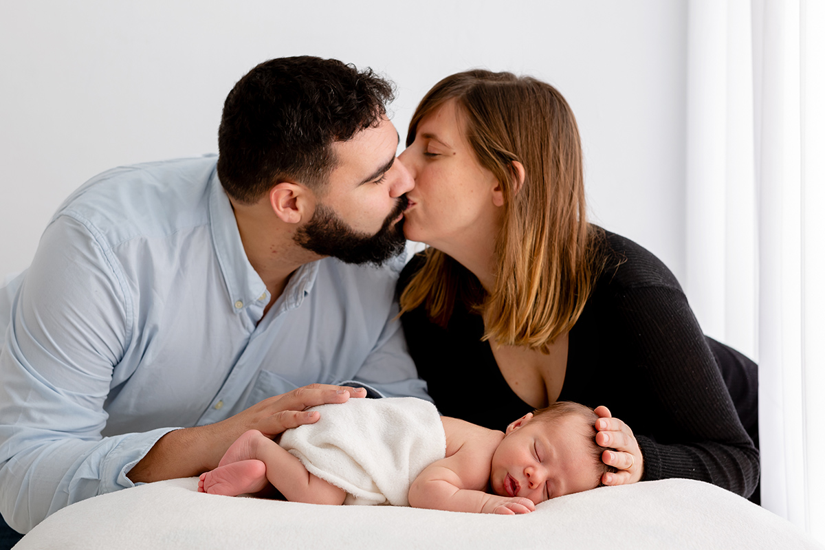 Papá y mamá dándose un beso mientras sostienen a su bebé recién nacido